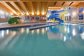 Une piscine intérieure avec un toboggan, une sculpture de grenouille et des poutres en bois au plafond.