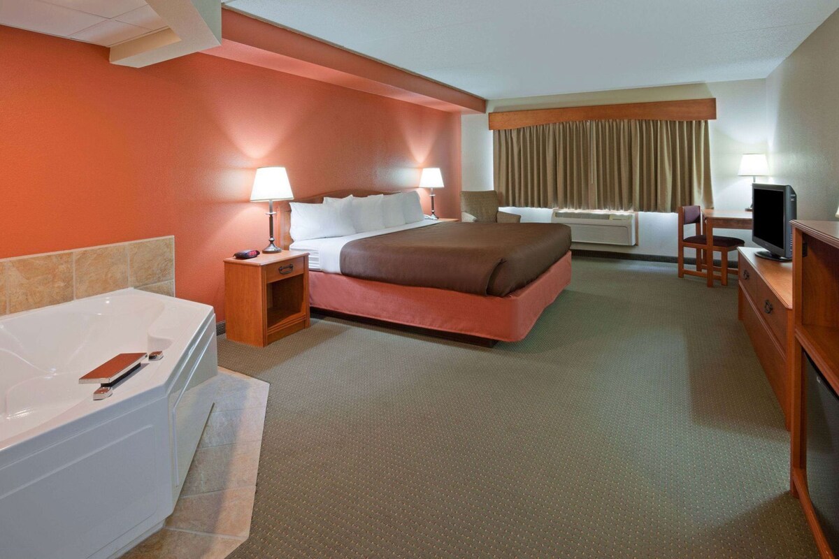 Ein Hotelzimmer mit einem großen Bett, einem eigenen Badezimmer mit Badewanne, einem Schreibtisch und einem Fernseher sowie einem Fenster mit Vorhängen.