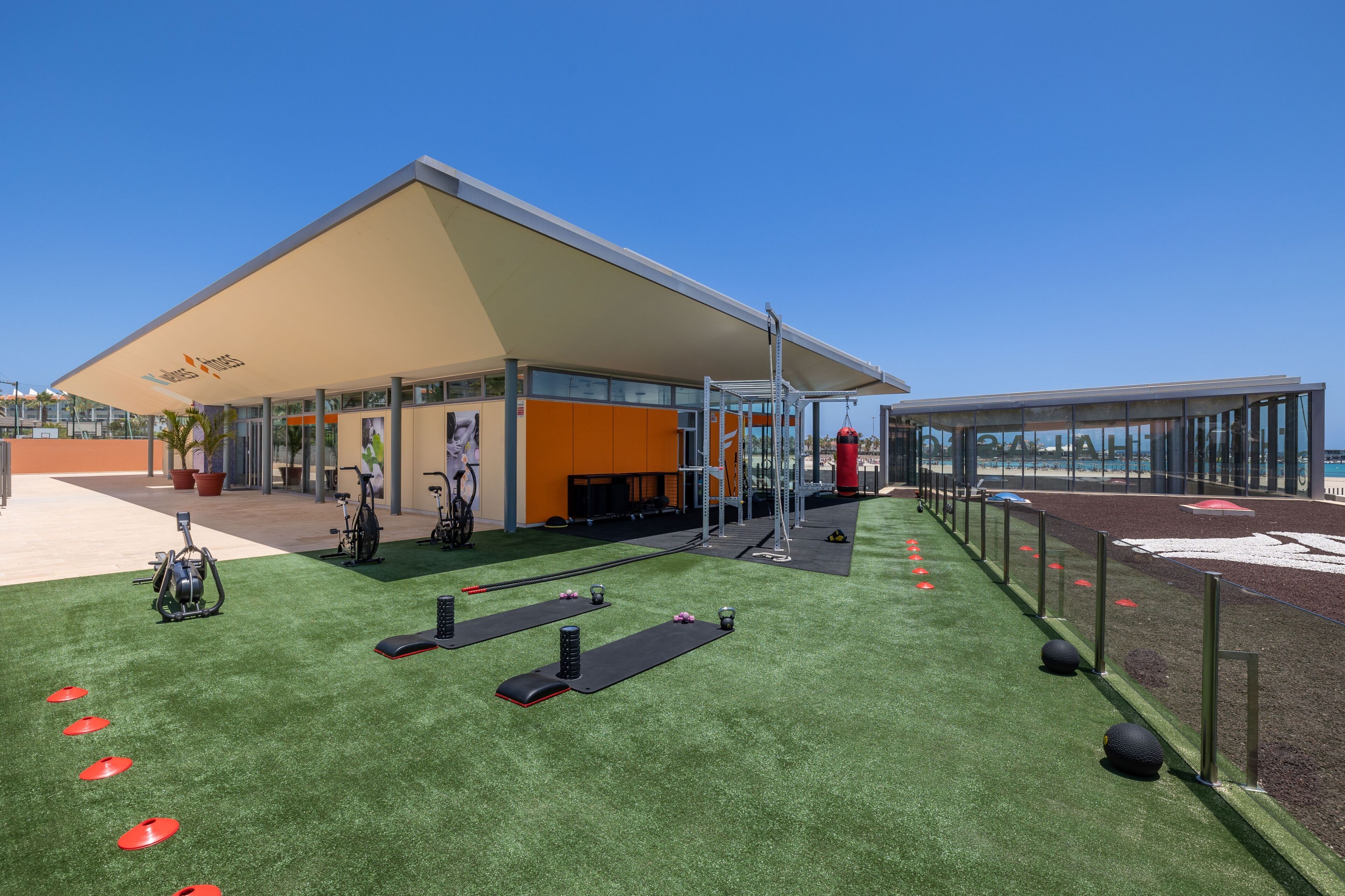 An outdoor gym area with exercise equipment, a covered seating area, and a clear sky.