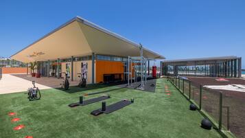 An outdoor gym area with exercise equipment, a covered seating area, and a clear sky.