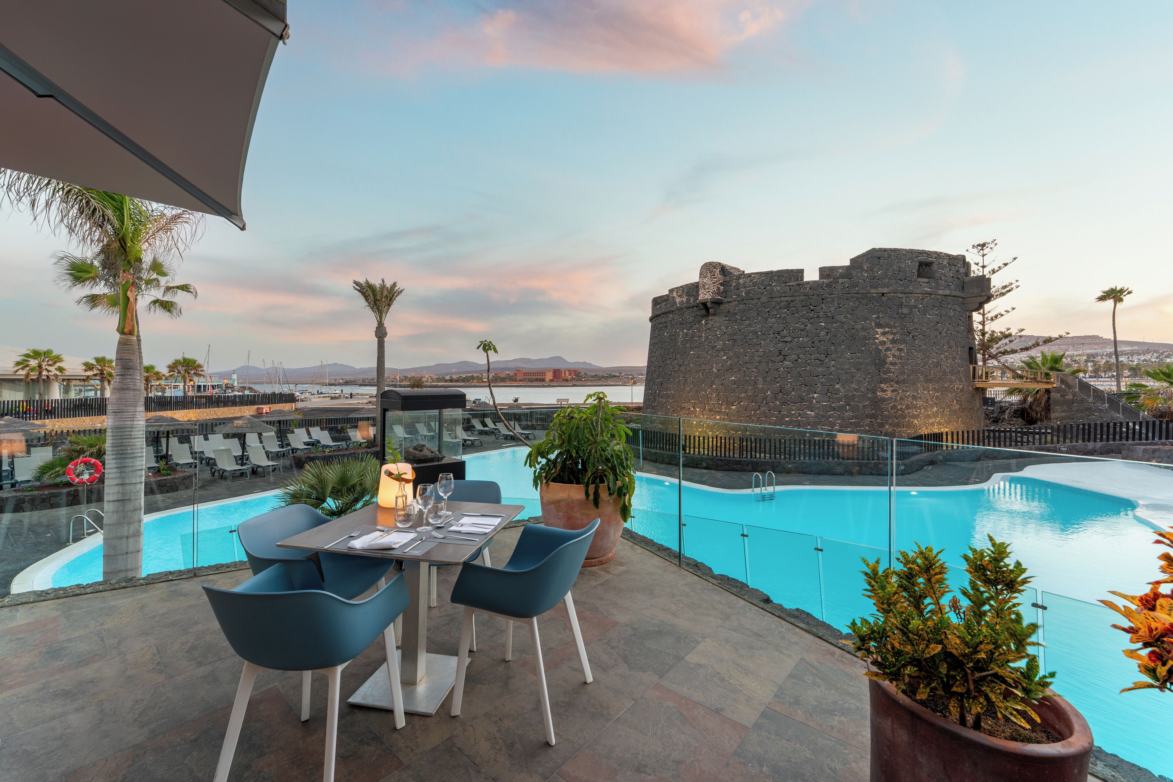 Un espace piscine aménagé sur le toit, avec une table et des chaises, une grande plante en pot et une structure en pierre en arrière-plan.