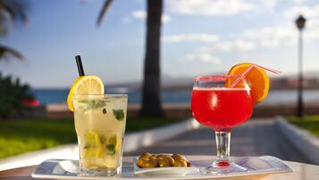 Two drinks on a tray with olives, set against a scenic background.