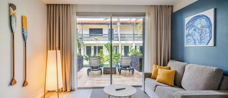 A modern living room with a sofa, a round coffee table, and a view of a balcony with outdoor furniture.