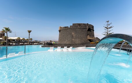 A swimming pool with clear blue water, a castle-like structure in the background, and a water fountain.