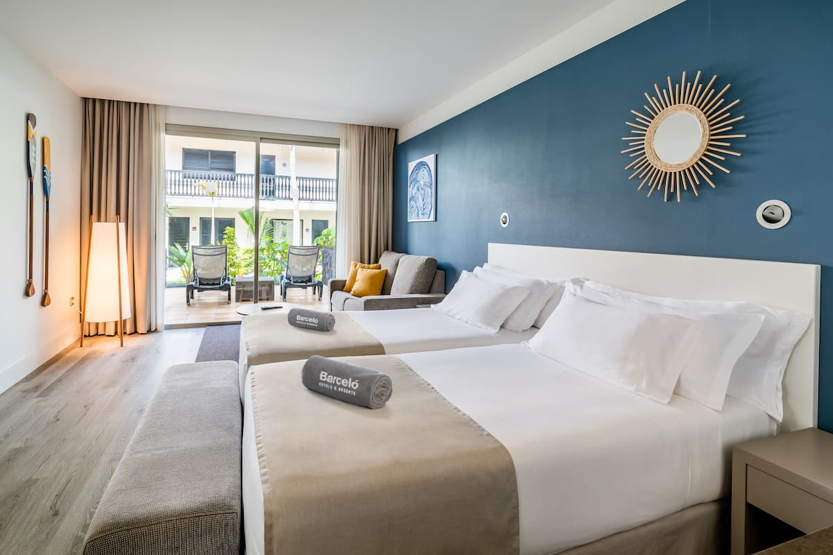 Ein Hotelzimmer mit zwei Betten, einem Spiegel mit Sonnenstrahlendesign, einem Balkon mit Stühlen und Blick auf das Gebäude.