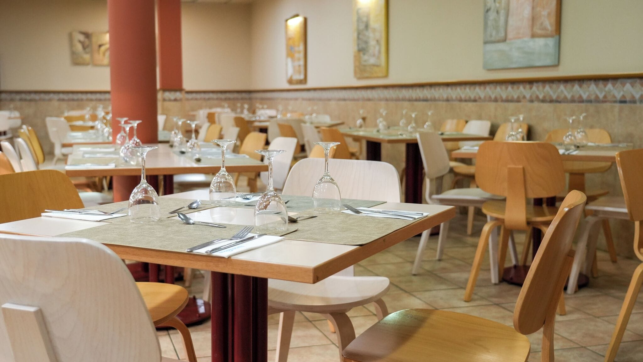 Un restaurant doté de nombreuses tables, chacune étant mise avec des couverts, des assiettes et des verres à vin.