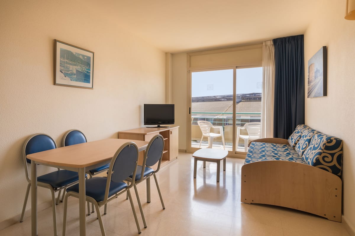 Une pièce comprenant une table à manger, des chaises, un canapé, un téléviseur et un balcon avec vue.