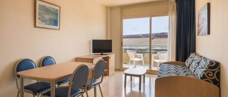 A room with a dining table, chairs, a sofa, a TV, and a balcony with a view.