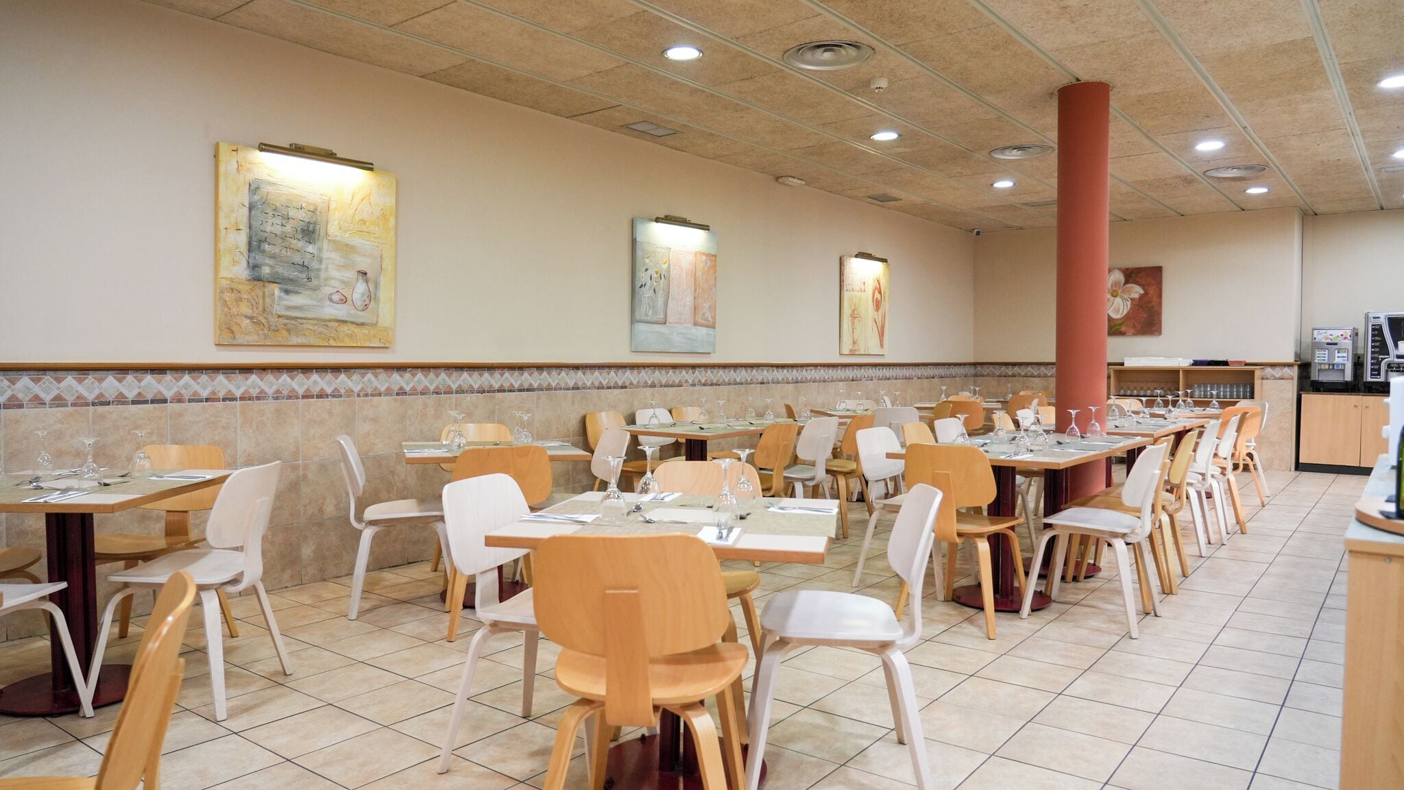 A restaurant with multiple tables and chairs, tiled floors, and artwork on the walls.