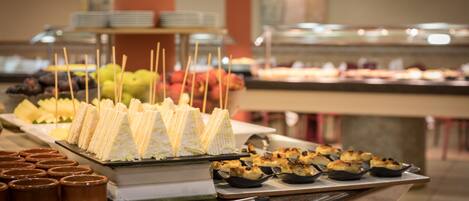 Un bufé con diversos alimentos, incluyendo sándwiches, frutas y pasteles.