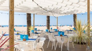 Restaurante à beira-mar com mesas ao ar livre, palmeiras e vista para a praia.