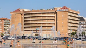 Um hotel com vários andares, varandas, estacionamento e área com uma fonte.