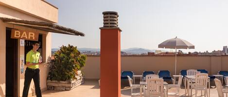 A rooftop terrace with outdoor seating, a bar, and a view of the cityscape.