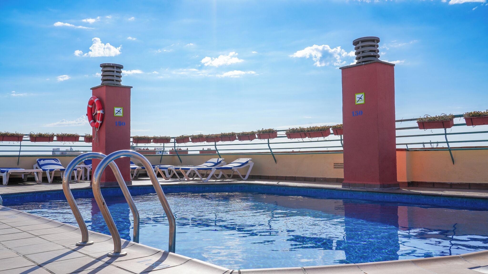 A pool with lounge chairs, lifebuoys, and potted plants.
