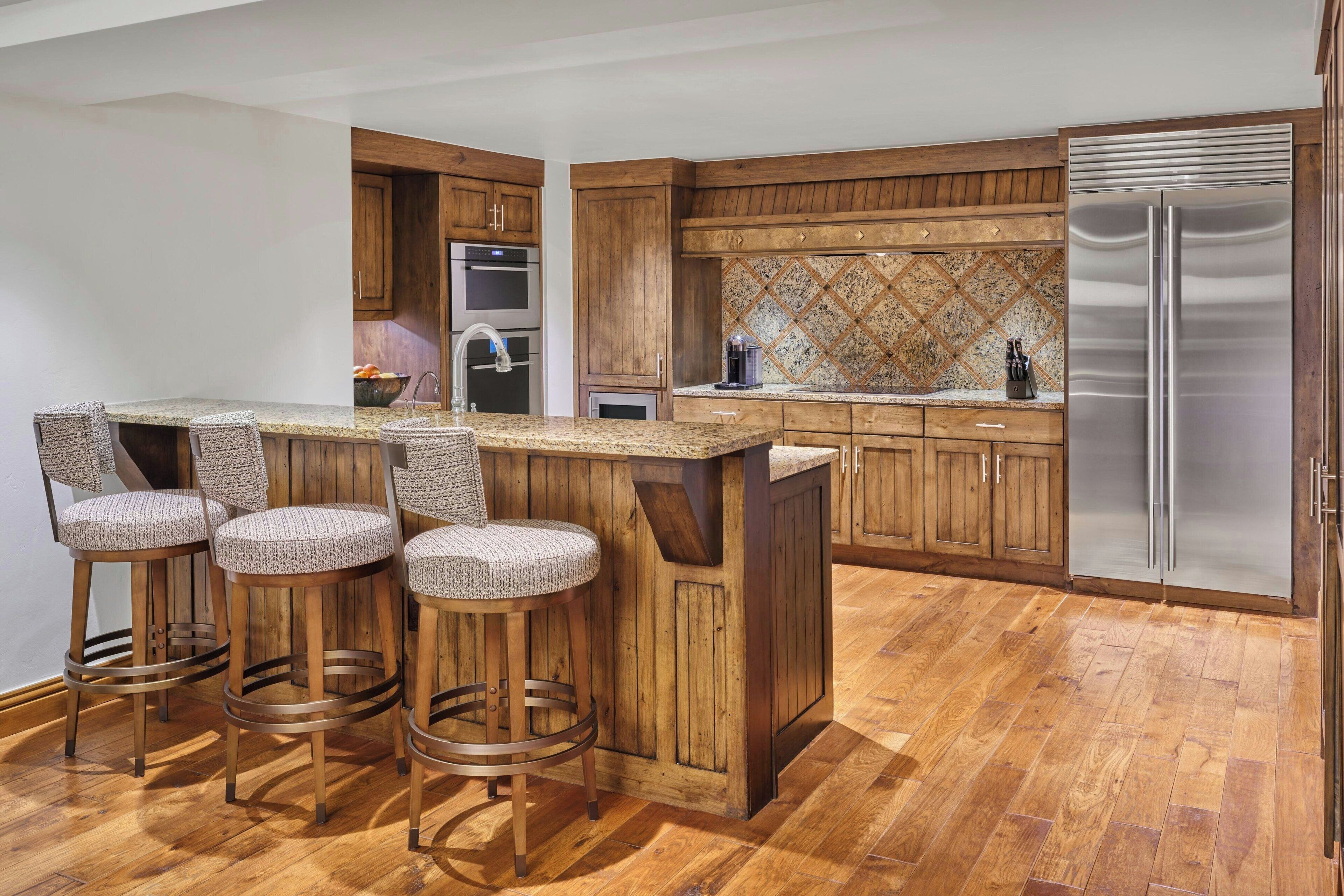 Cocina con armarios de madera, refrigerador de acero inoxidable y una barra con taburetes.