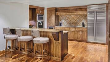Cocina con armarios de madera, refrigerador de acero inoxidable y una barra con taburetes.