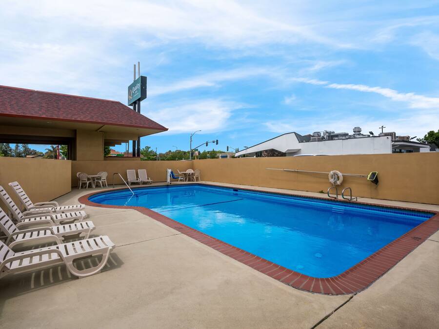 A swimming pool with lounge chairs and a covered area, surrounded by a low brick wall and a building with a red roof.