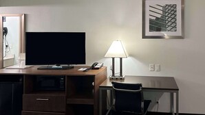 Habitación de hotel con escritorio, televisor de pantalla plana, lámpara, teléfono y una silla.