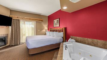 A hotel room with a bed, a fireplace, a large window with curtains, a red wall, and a bathtub.