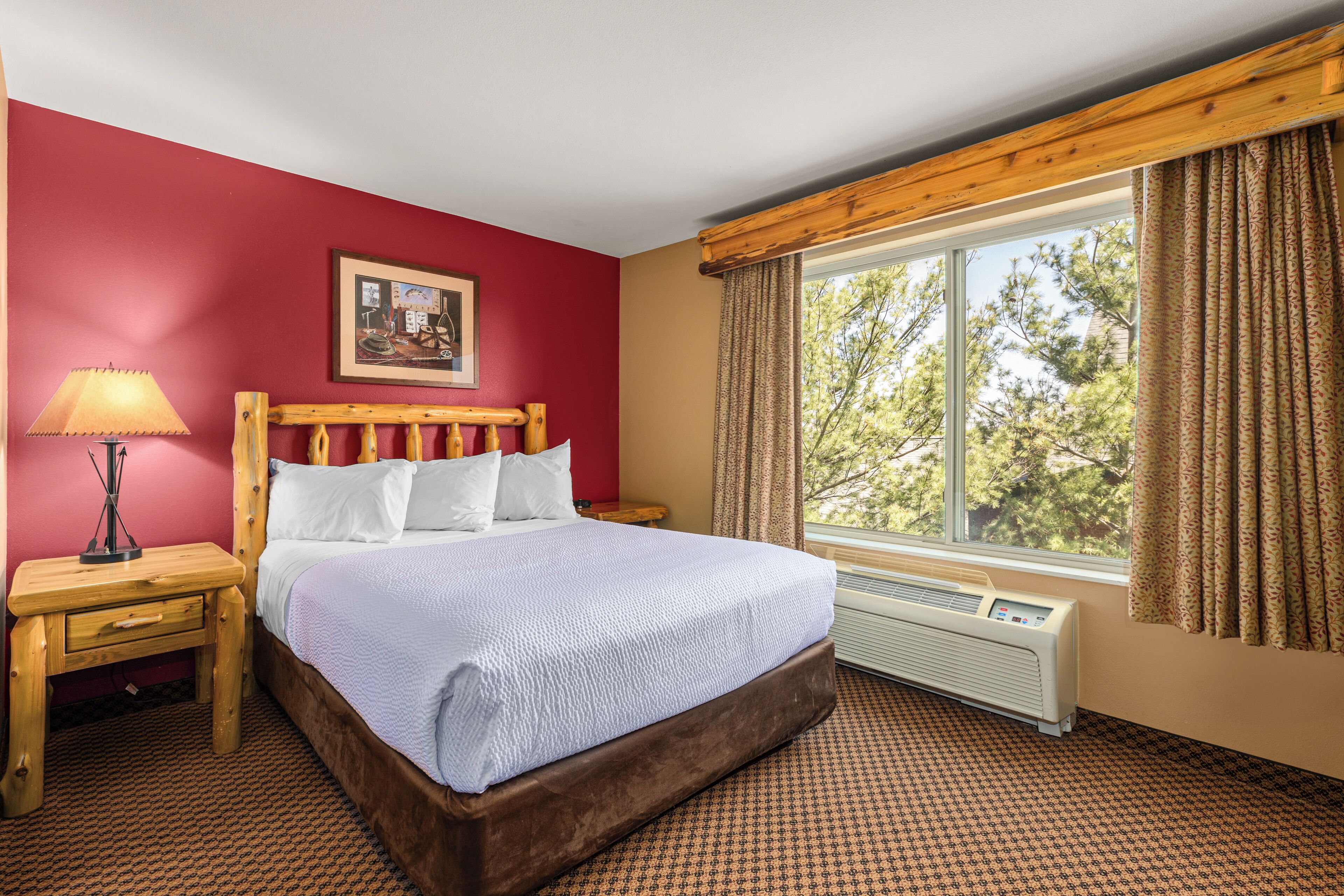 A hotel room with a bed, a nightstand, a lamp, a window with curtains, and a radiator.