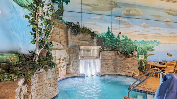 An indoor pool with a waterfall feature, stone walls, and a mural of a natural landscape. - The Lodge at Brainerd Lakes, Trademark Collection by Wyndham (Brainerd)