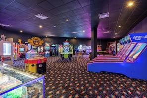 Une salle d’arcade intérieure comprenant divers jeux, un tapis à motifs et un espace détente avec des sièges bleus.