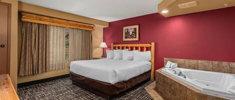 A hotel room with a bed, a large window with curtains, a wooden headboard, a bathroom with a bathtub, and a patterned carpet.