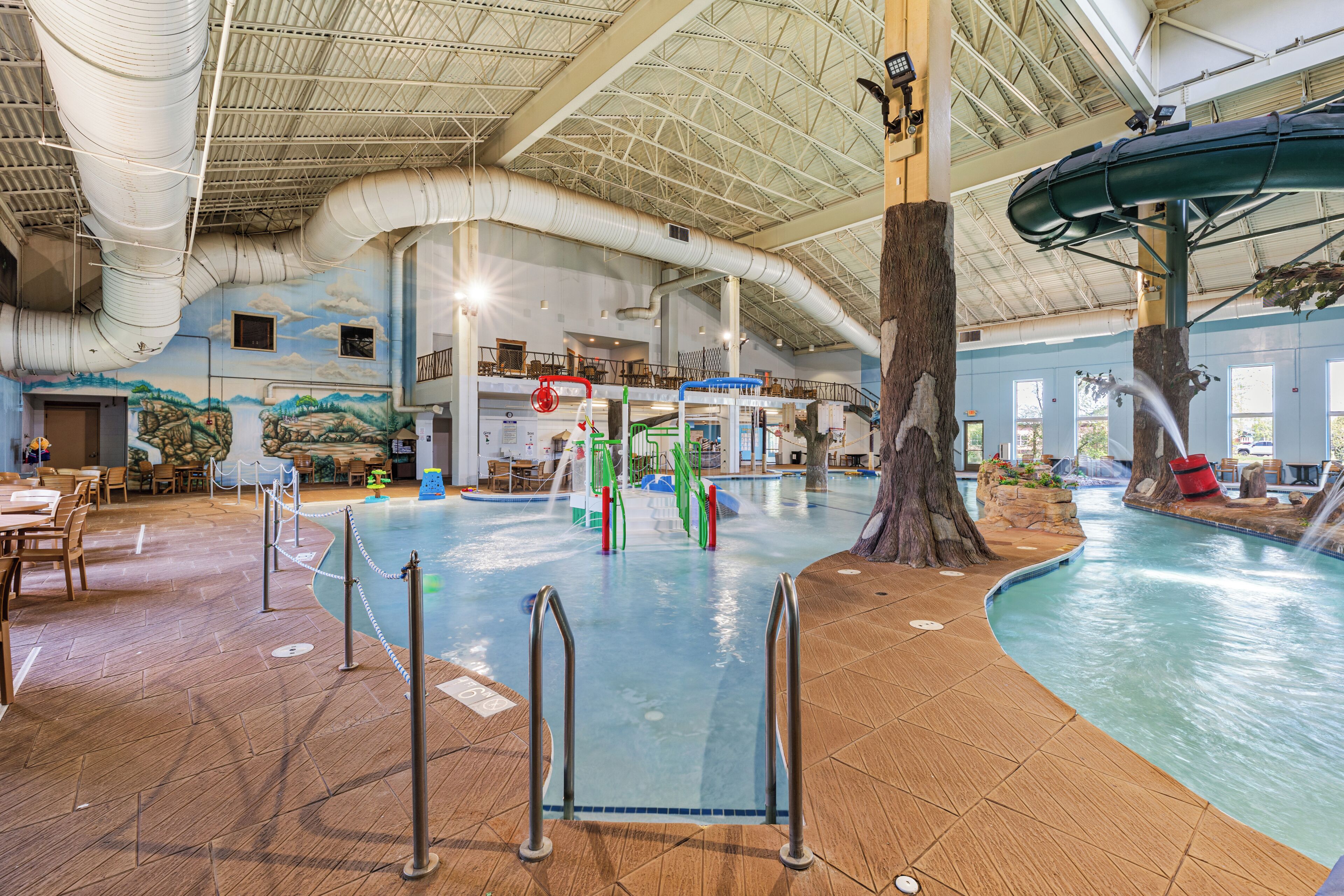 Una piscina interior con tobogán, un árbol y un mural en la pared.