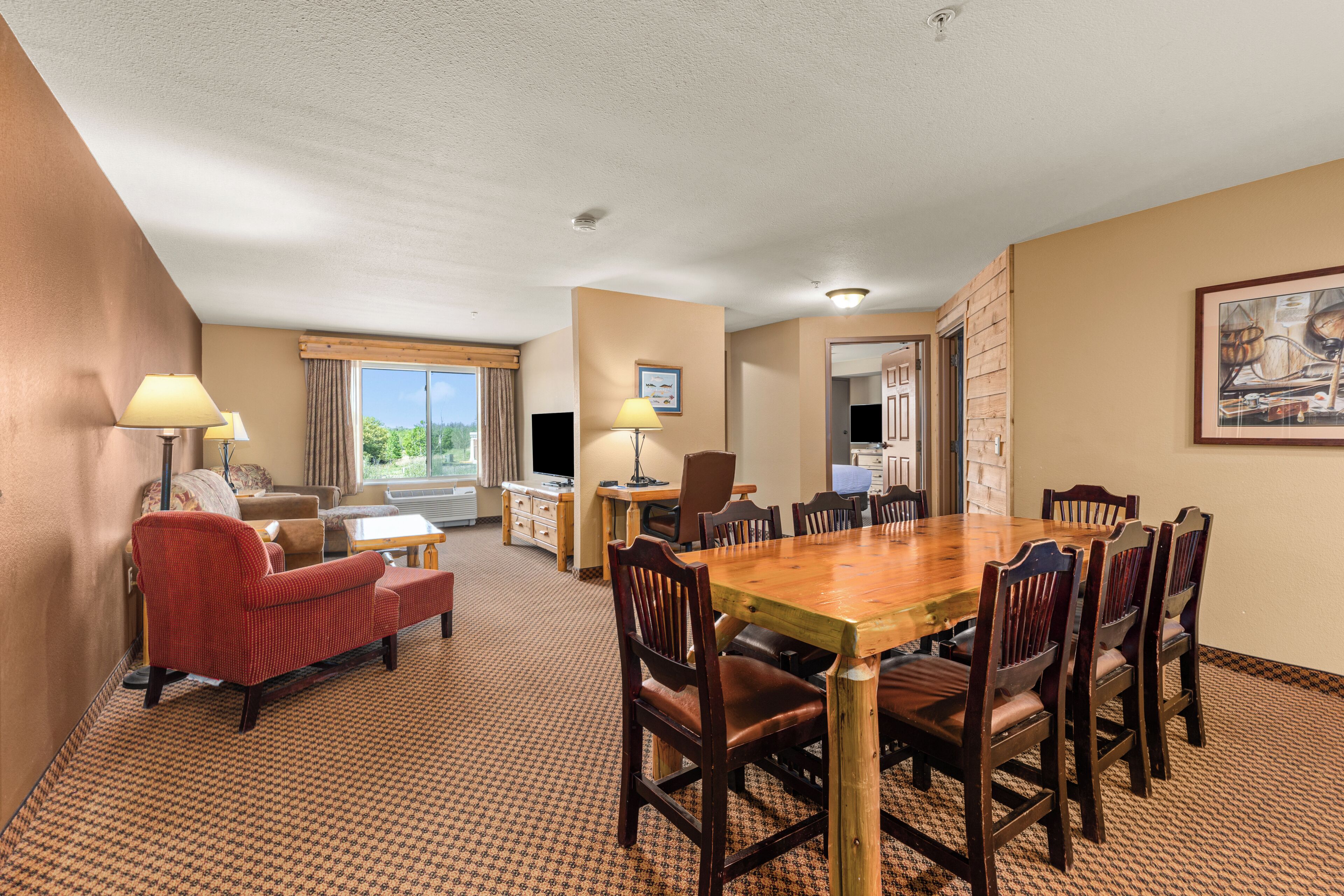 A hotel room with a dining area, a sofa, a TV, and a window with curtains.