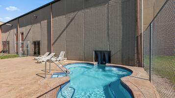 A swimming pool with a tiled edge, surrounded by a fence, and adjacent to a building with a metal exterior.