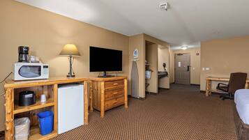 A hotel room with a wooden desk, a television, a lamp, a bed, a small refrigerator, and a trash bin.