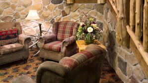 A staircase with wooden railings, a stone wall, and a fireplace. There are two upholstered chairs and a lamp. - The Lodge at Brainerd Lakes, Trademark Collection by Wyndham (Brainerd)