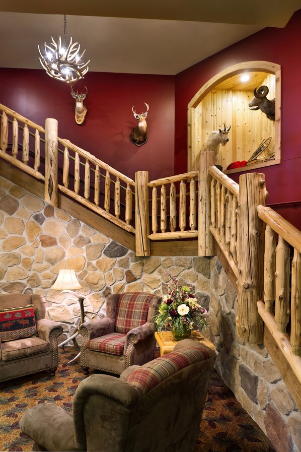 A staircase with wooden railings, a stone wall, and a fireplace. There are two upholstered chairs and a lamp.