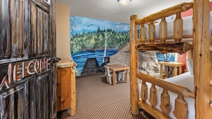 A rustic room with a welcome sign, a mural of a forest, a bed, a table, and a bench. - The Lodge at Brainerd Lakes, Trademark Collection by Wyndham (Brainerd)