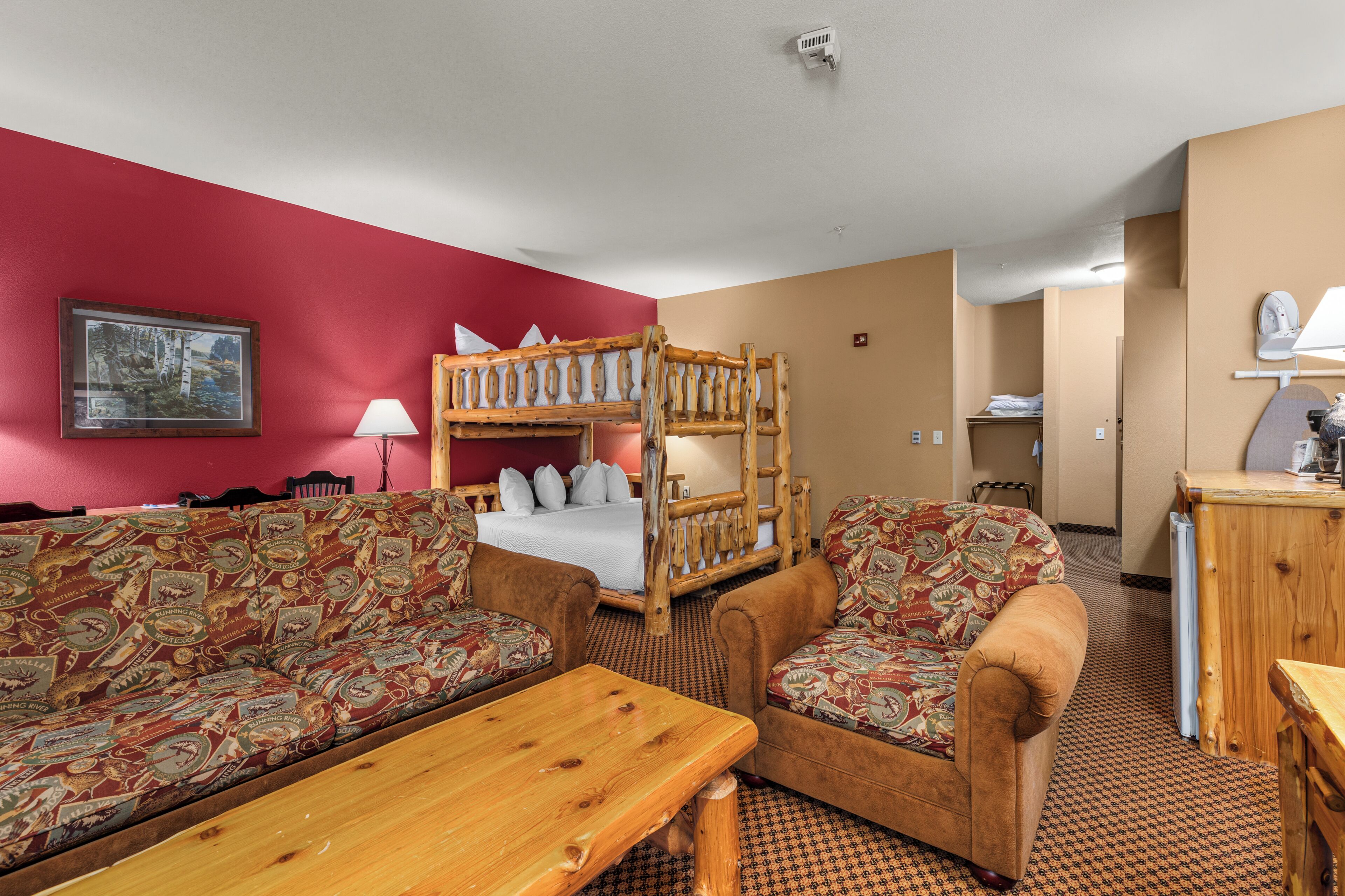 Hotelkamer met een stapelbed, twee gestreepte banken, een houten tafel en een rode muur met een lijstwerk.