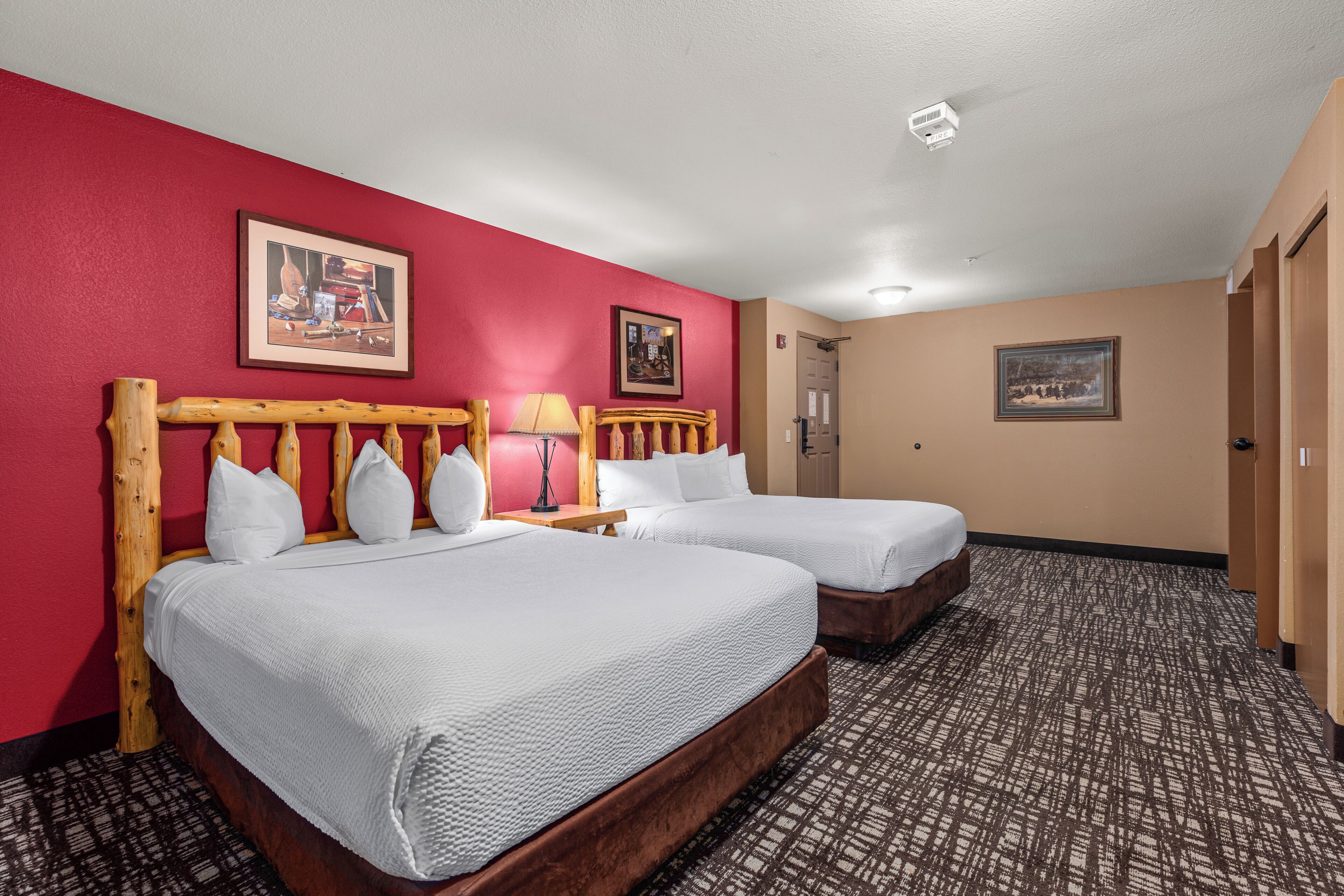 A hotel room with two beds, a red wall, and a patterned carpet.