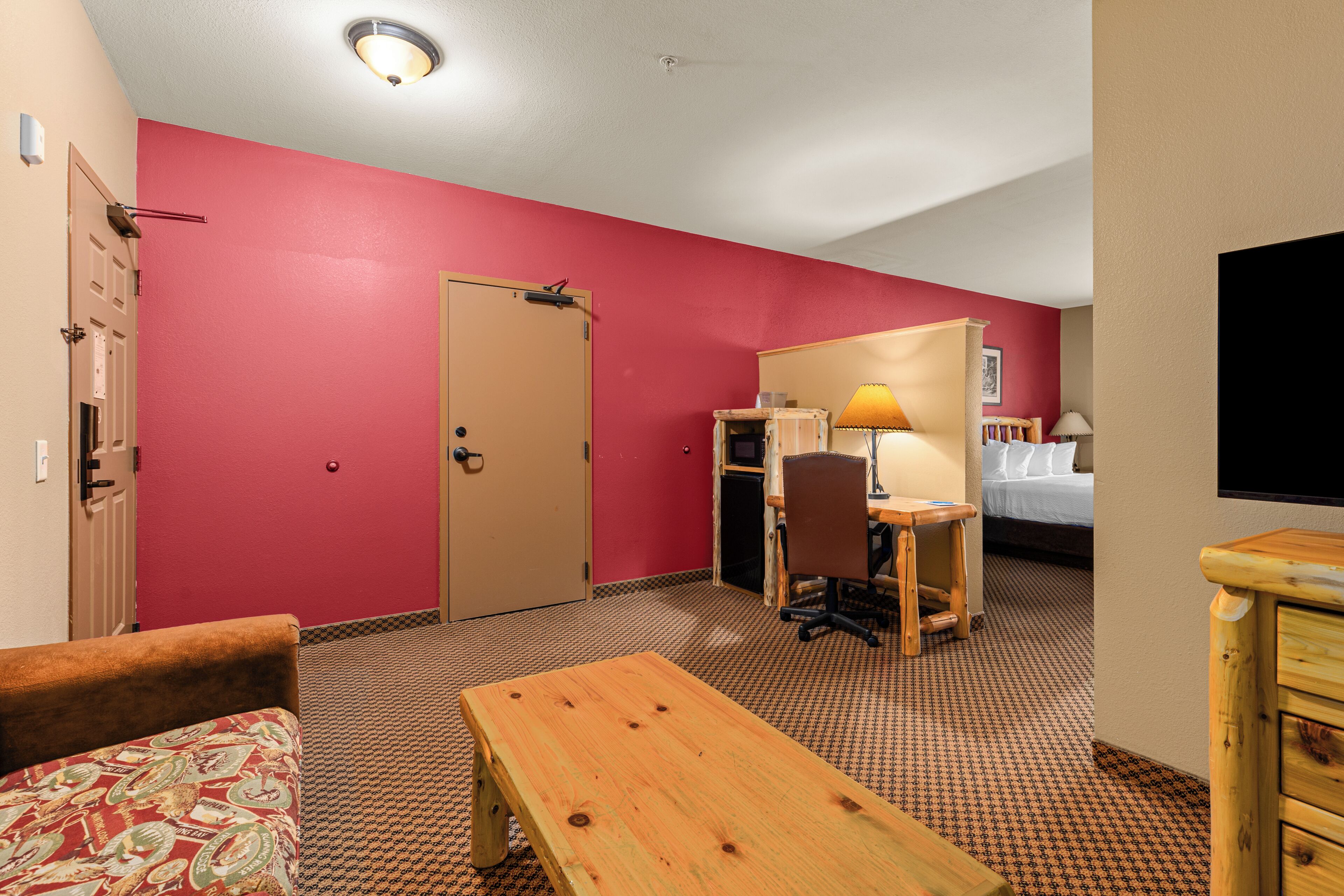 A hotel room with a bed, a desk with a chair, a wooden table, a sofa, and a television.