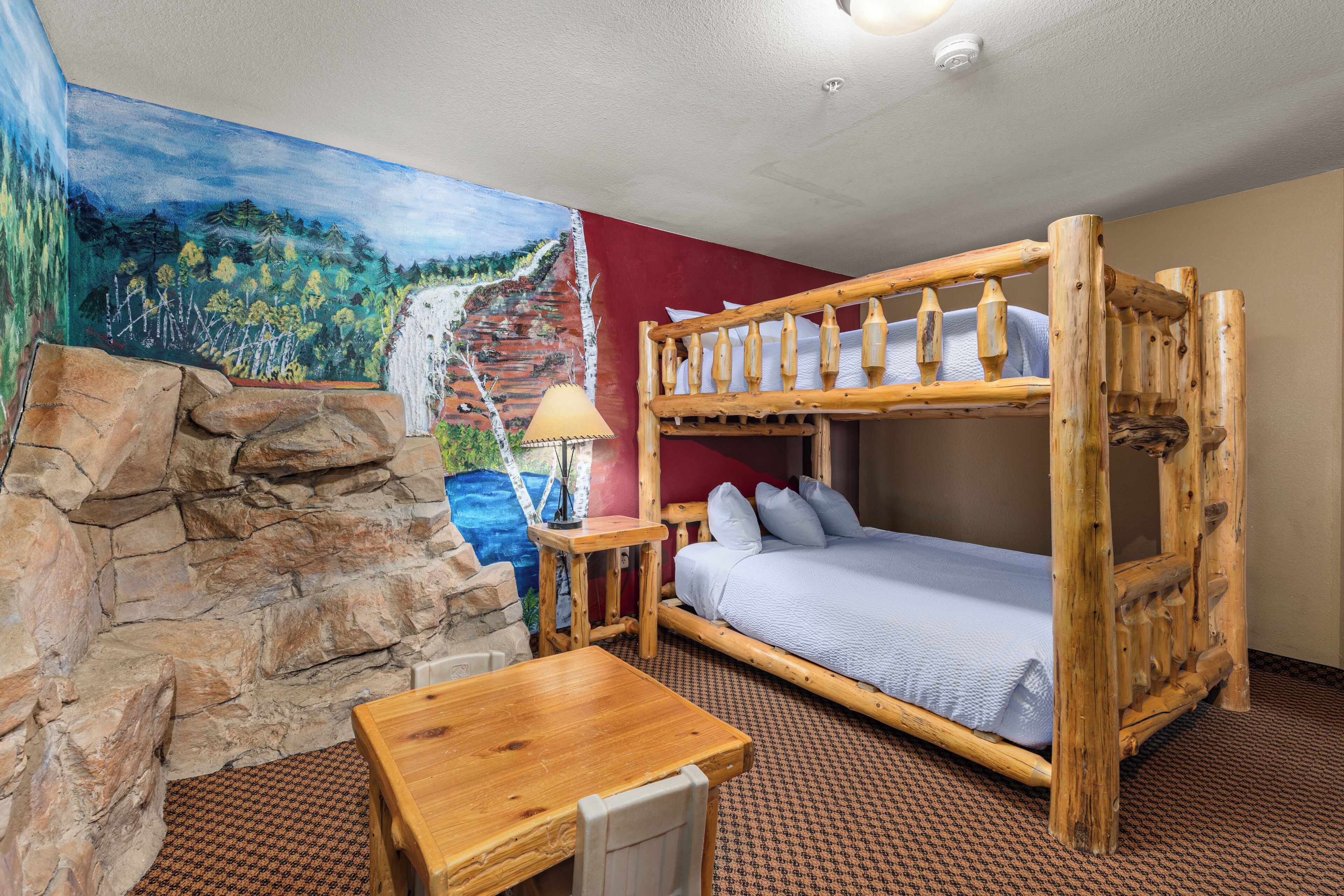 Una cama litera con estructura de madera, una mesita, una lámpara y una pared de piedra.
