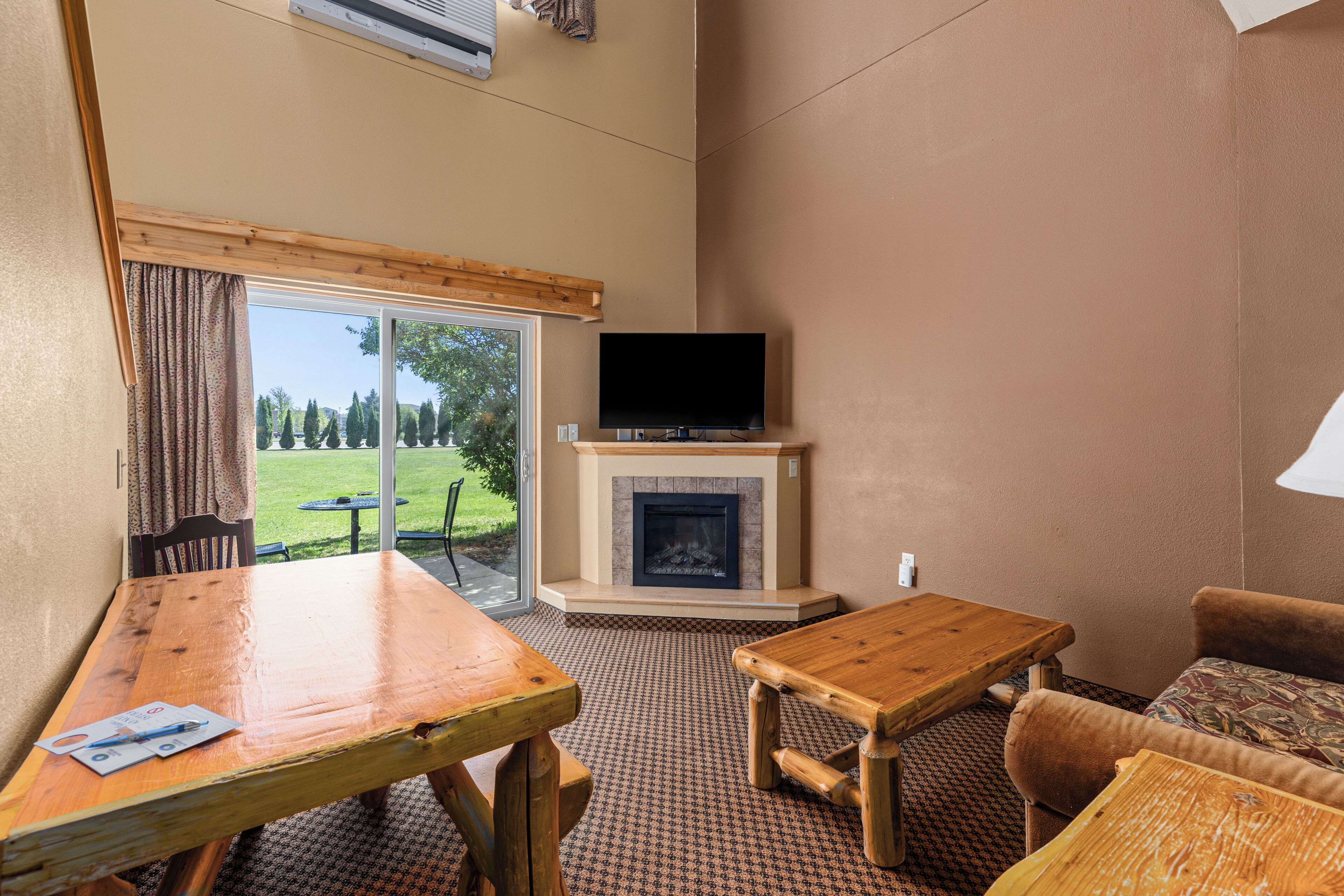 A room with a wooden table, a sofa, a fireplace, and a television.