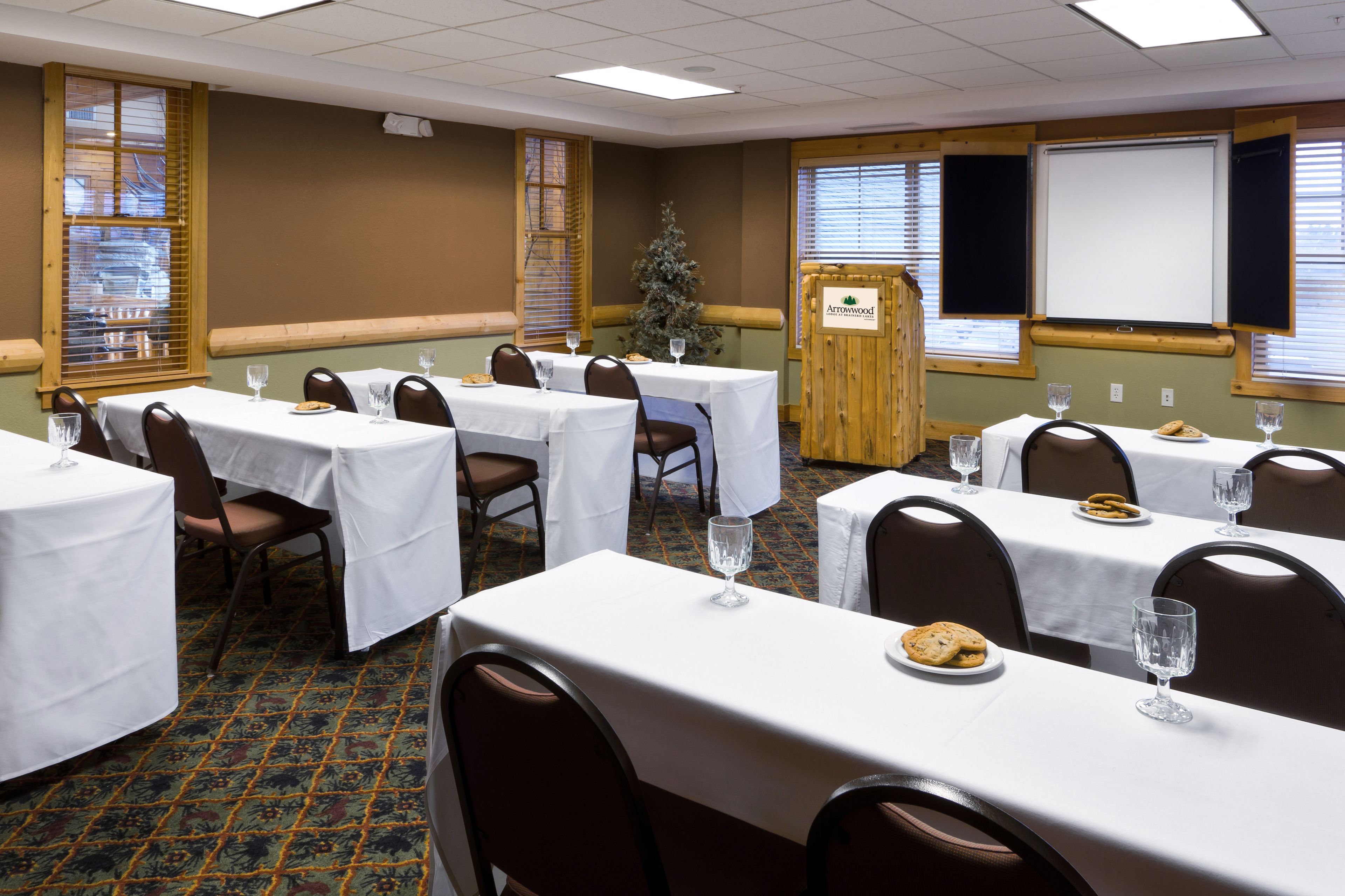 A conference room with multiple tables, each with a white tablecloth, chairs, and a small Christmas tree.