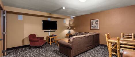 A hotel room with a sofa, armchair, wooden table, lamp, and a flat-screen TV mounted on the wall.