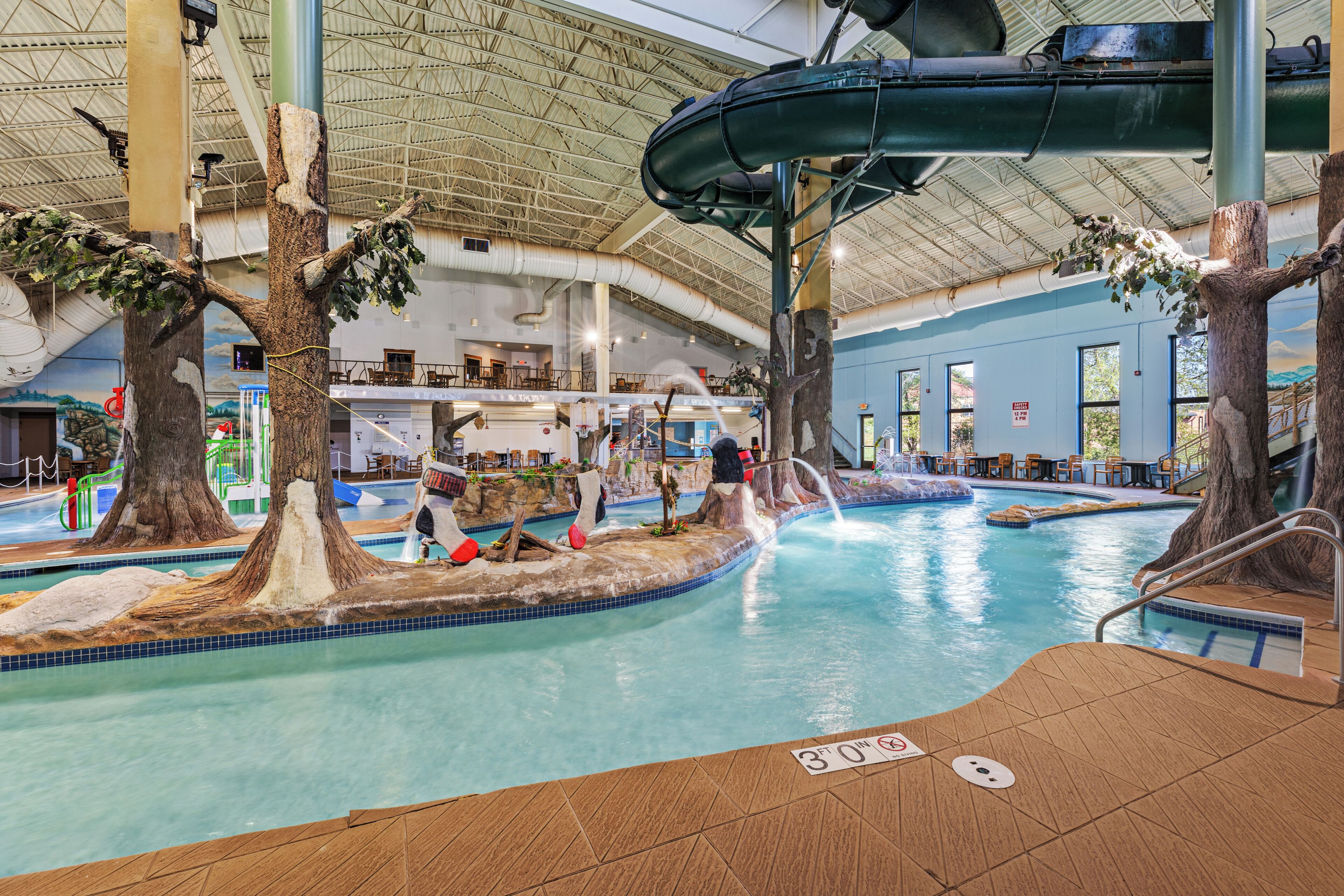 An indoor pool with a water slide, artificial trees, and a lifeguard station.