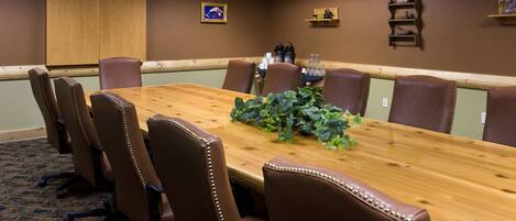 Una sala de conferencias con una mesa de madera, sillas de cuero marrón, una planta en maceta y una estación de café.