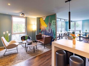 A modern hotel room with a large window, a seating area with a sofa and chairs, a small table, and a decorative wall with a geometric pattern. - B&B Hotel Hannover-Lahe (Hannover)
