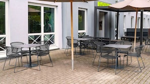 An outdoor seating area with tables and chairs, a reception sign, and a building facade. - B&B Hotel Hannover-Lahe (Hannover)