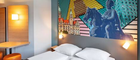A hotel room with a bed, two pillows, a nightstand, a lamp, and a wall mural.