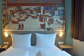 A hotel room with a large bed, two bedside tables, and a wall-mounted artwork depicting a vintage map. - Premiere Classe Berlin-Dreilinden (Kleinmachnow)