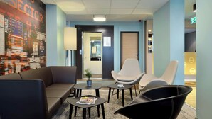 A modern lounge area with seating, a coffee table, and a wall with directional signs. - Premiere Classe Berlin-Dreilinden (Kleinmachnow)