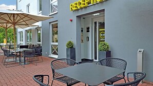 A reception area with a sign, outdoor seating, and a building entrance. - Premiere Classe Berlin-Dreilinden (Kleinmachnow)