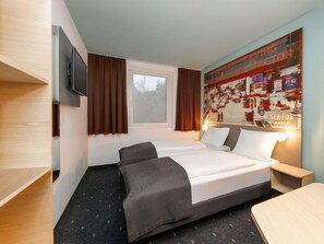 Hotelkamer met een bed, een aan de muur bevestigde televisie, een raam met gordijnen en een poster aan de wand.